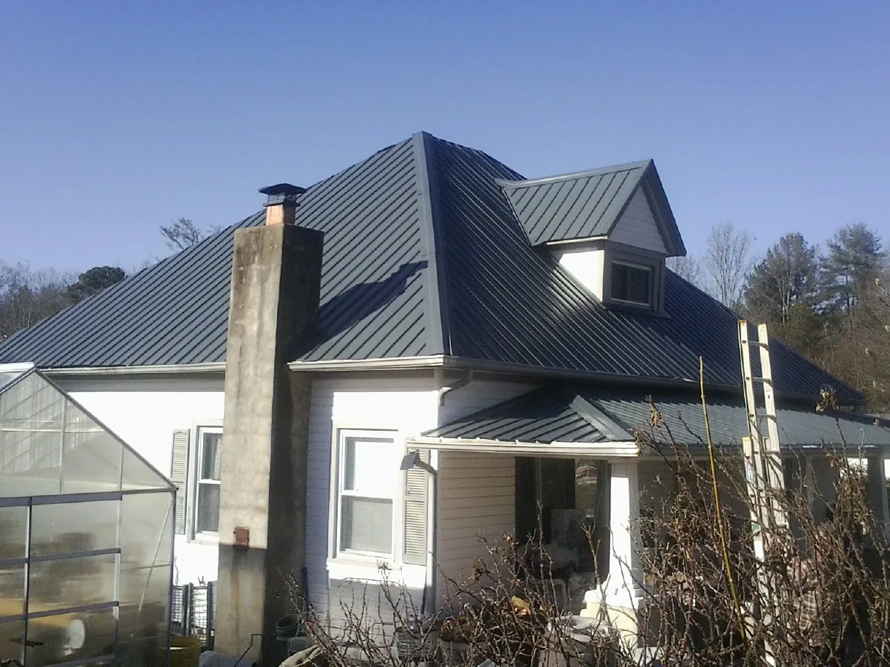 Dark blue standing seam metal roof on a white farmhouse with dormer — Slate & Tile Roof Repair by Roofing Brothers in Shafer