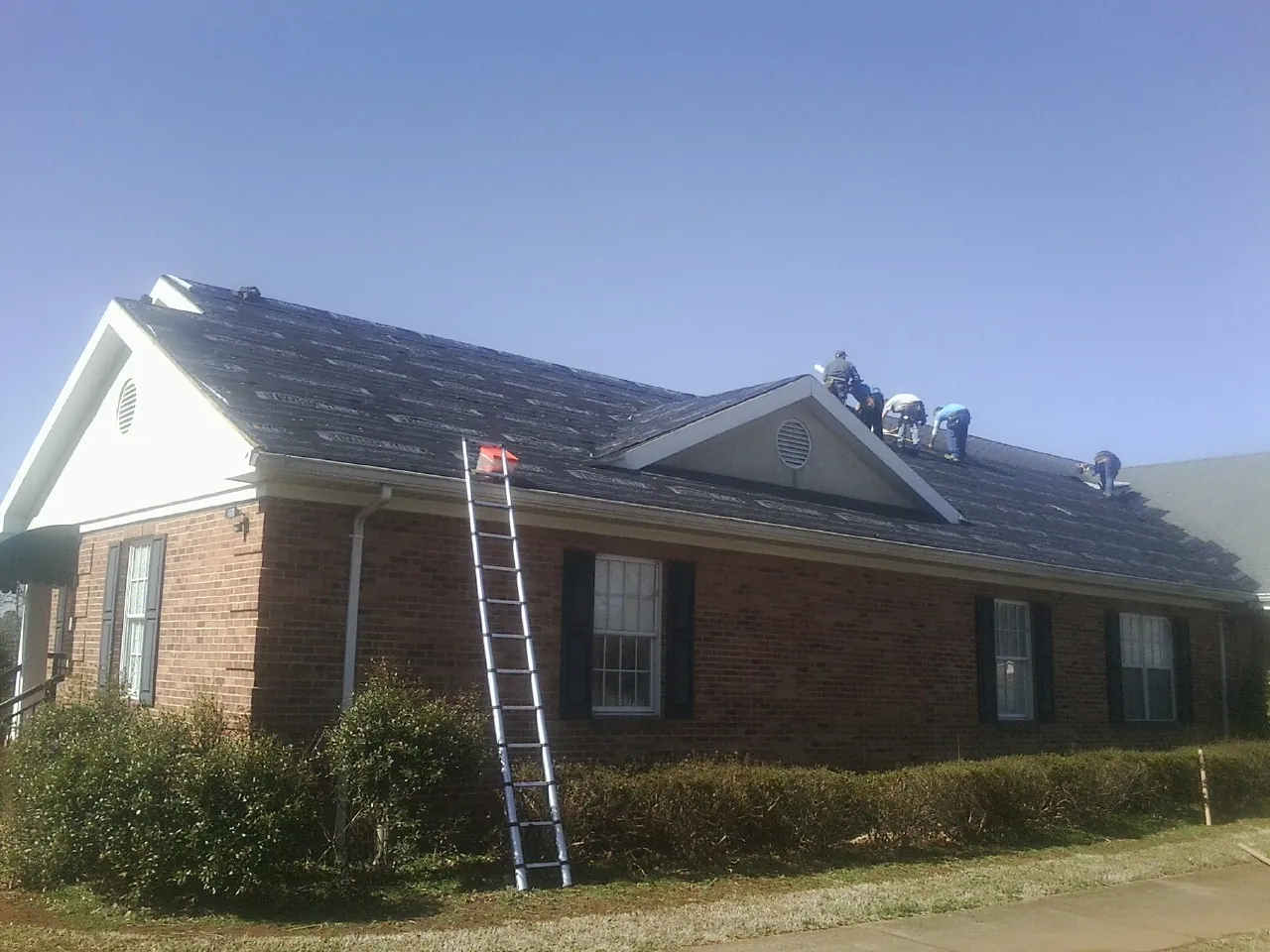 Crew tearing shingles off a brick ranch roof with a ladder set — Emergency Roof Repair work by our crew in Shafer