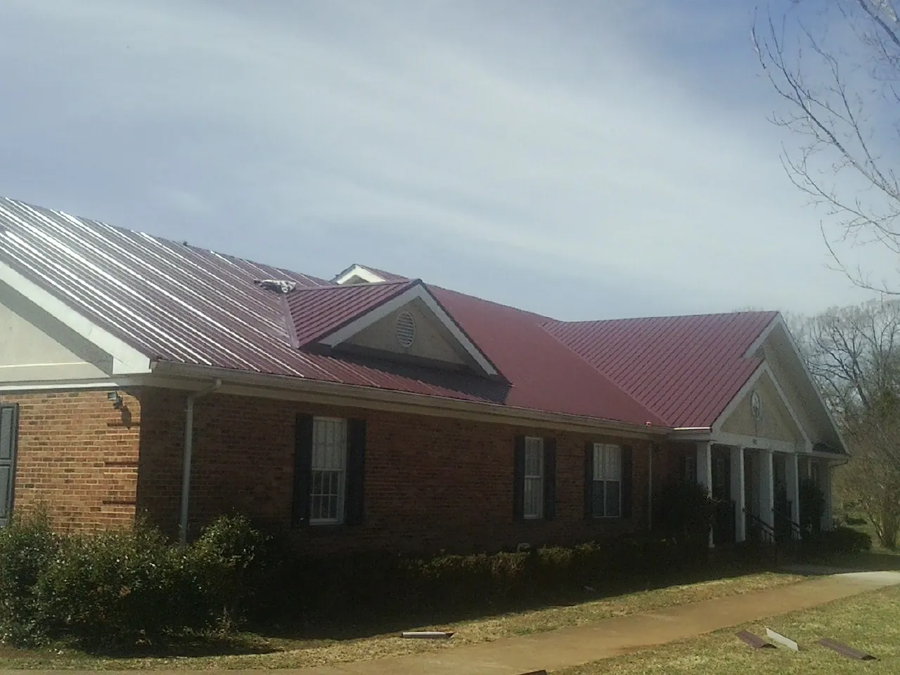 Red metal roof with gabled entries on a long brick building, from a Hail Damage Roof Repair job in Shafer