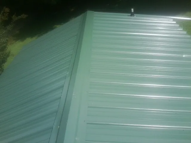 New green metal panels meeting at the ridge of a roof — Flat Roof Repair work by our crew in Shafer