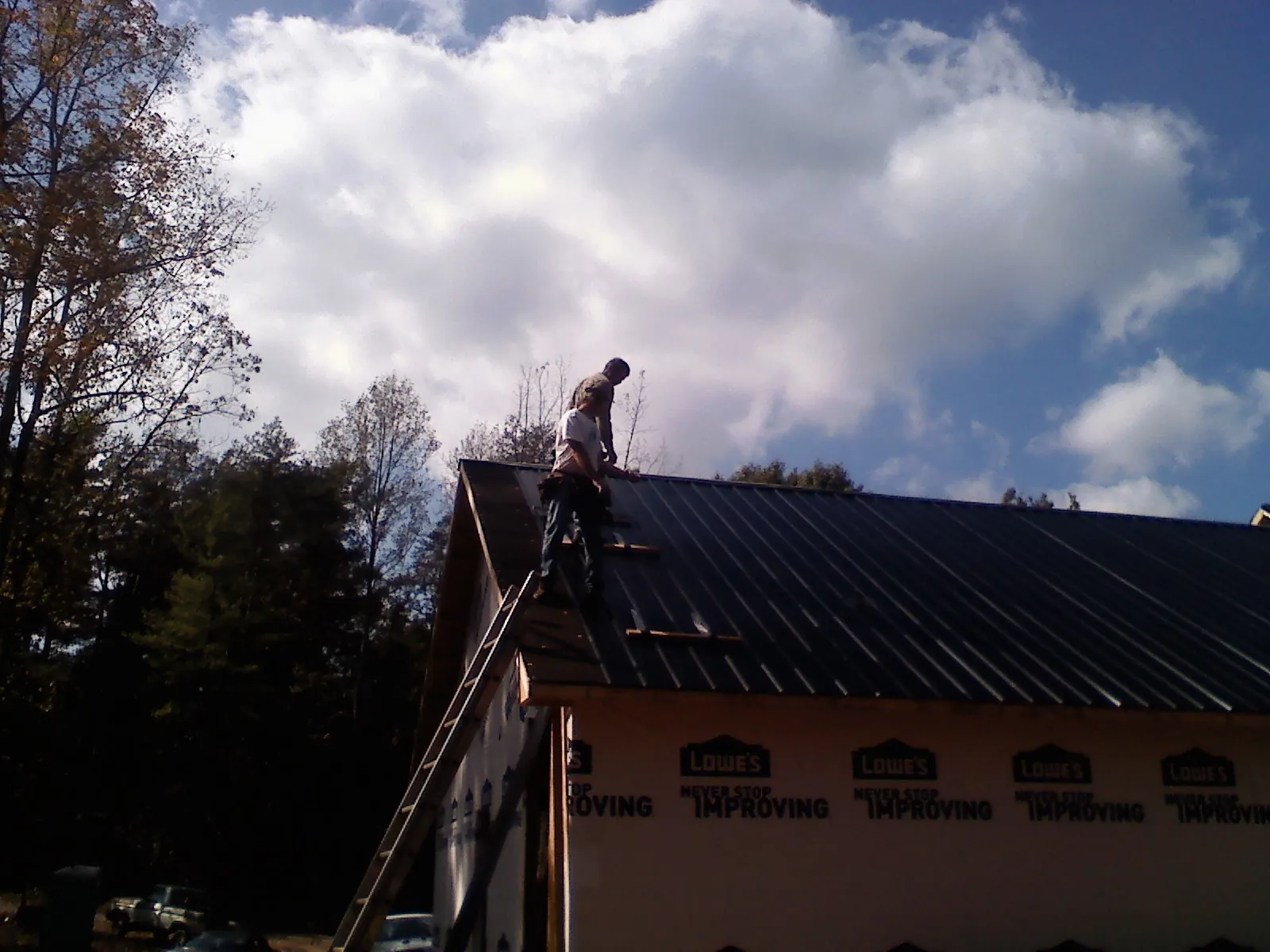 Roofer fastening dark metal panels high against a cloudy sky, from a Roof Inspection job in Shafer