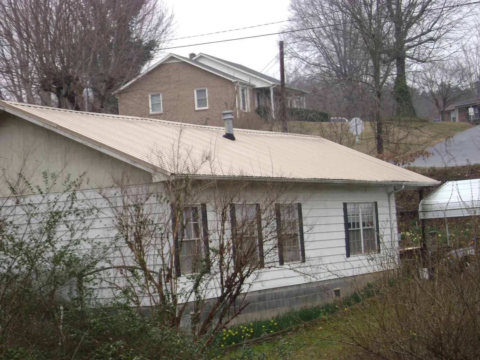 Tan metal roof on a white sided house set into a hillside — Commercial Roofing by Roofing Brothers in Shafer